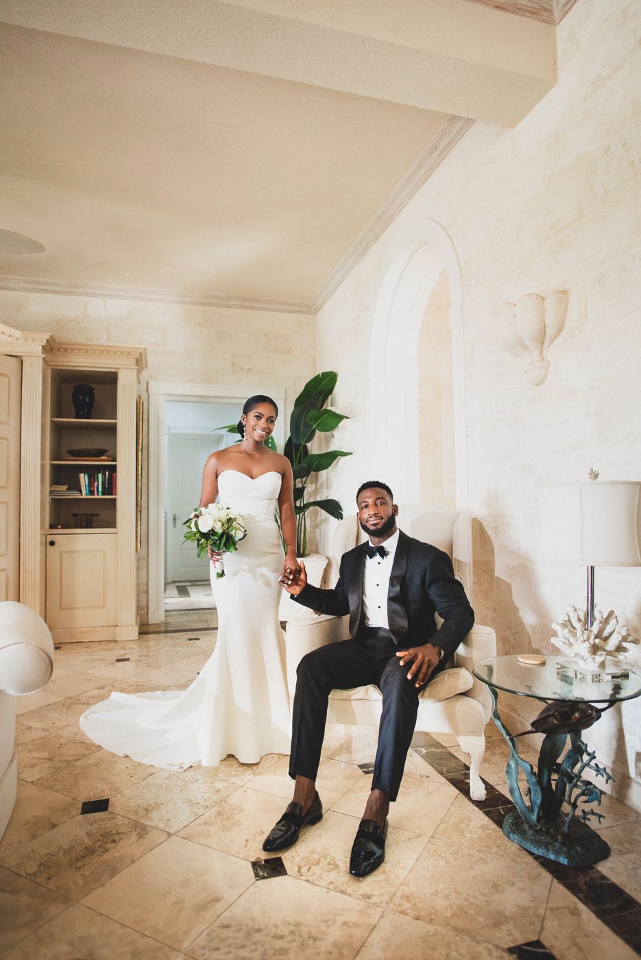 Elegant wedding portrait in a luxurious indoor setting with tropical plants and classic decor.