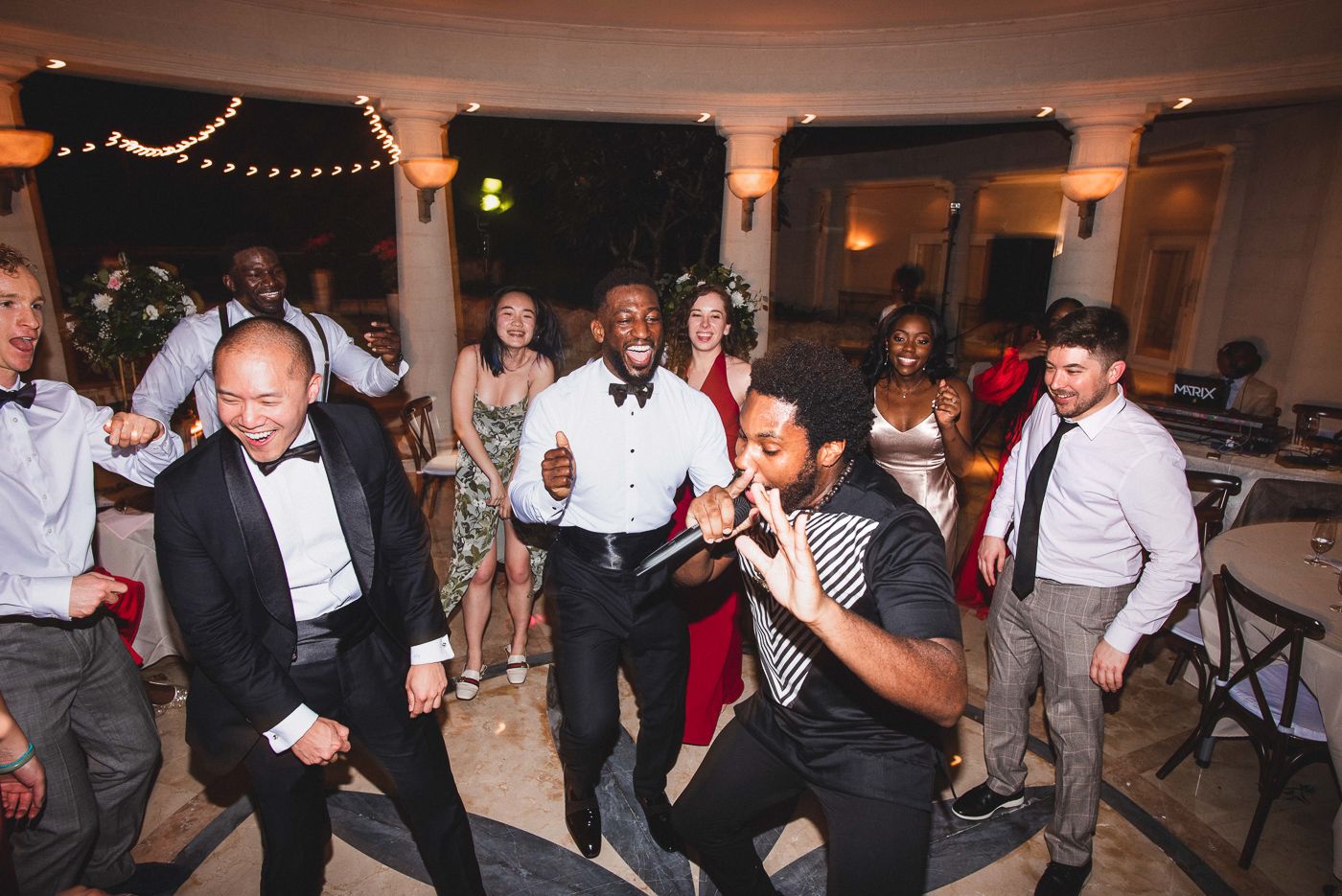 Wedding celebration with guests dancing in an elegantly lit indoor venue.