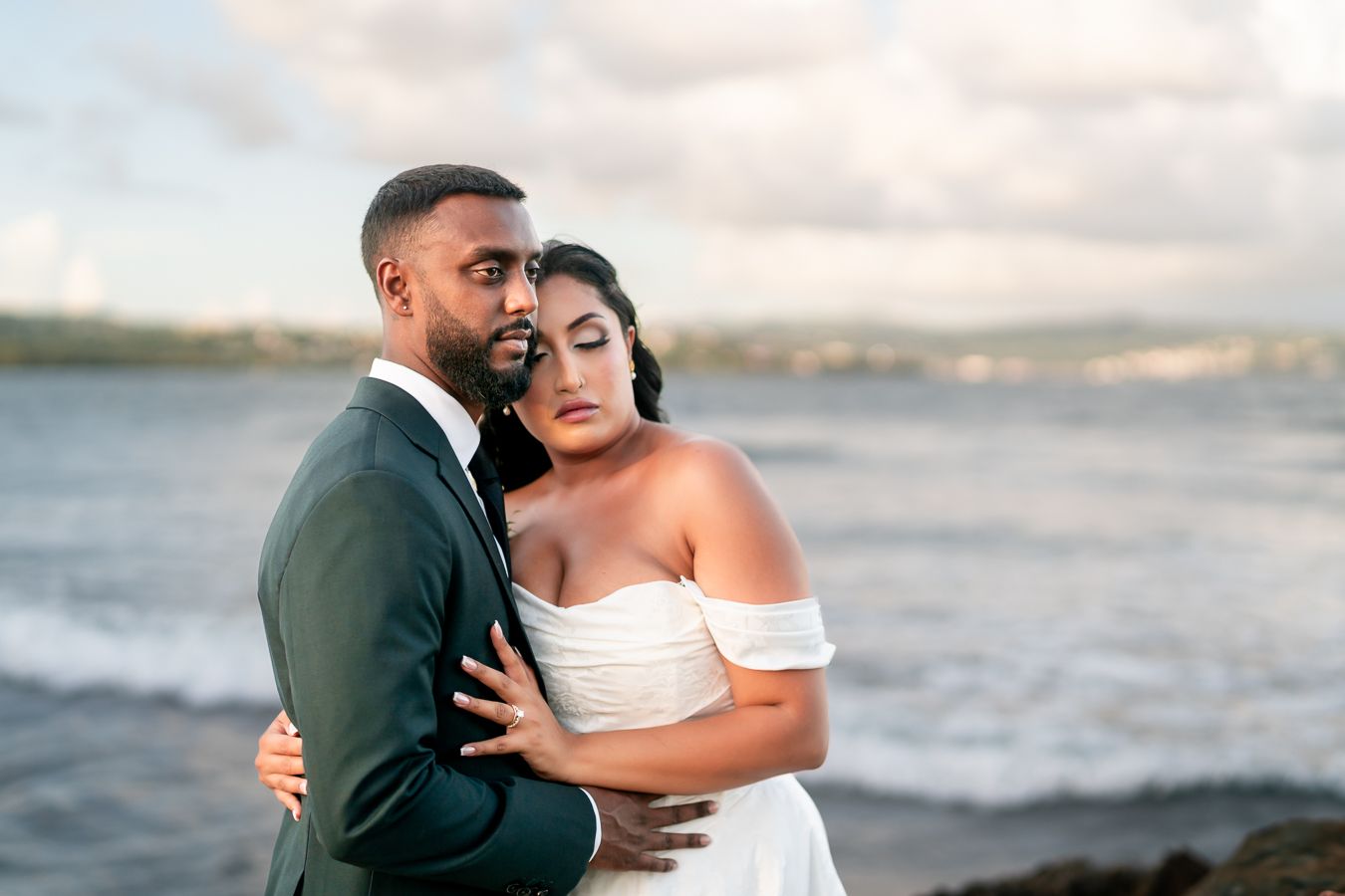 Romantic beachside wedding portraits with waves crashing against rocky shoreline at sunset.