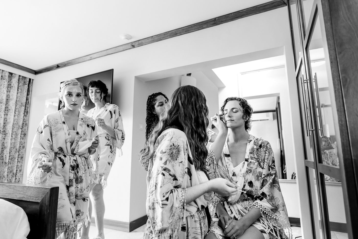 Black and white photo of wedding party in floral robes getting ready together.