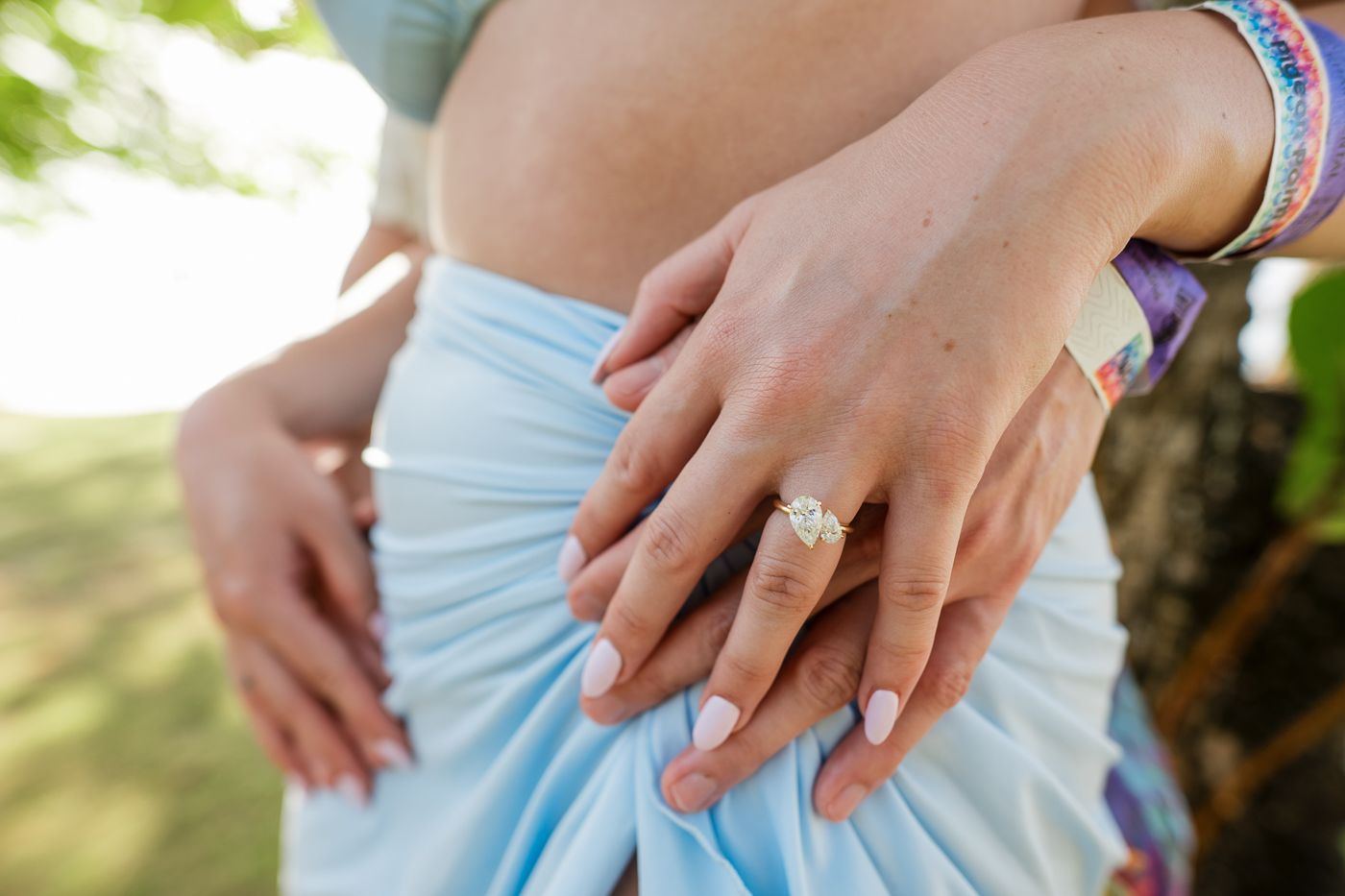 Close up of engagement ring and hospital wristbands in outdoor setting showing hands.