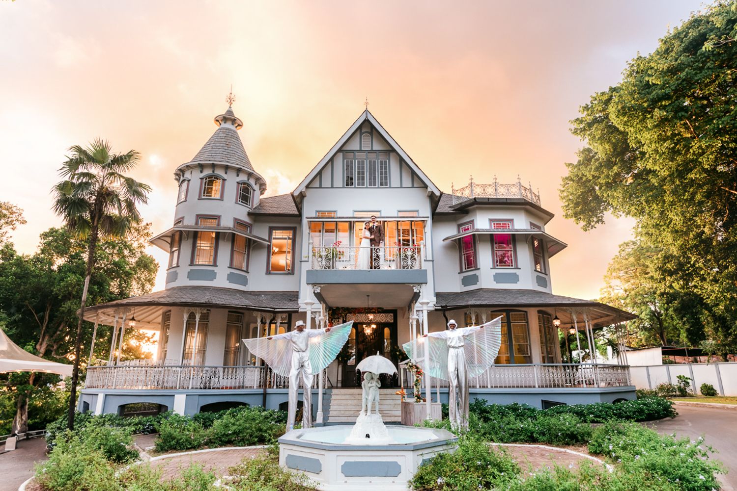 Victorian-style architecture showcases white cottage with wrap-around porch and tower against sunset sky.