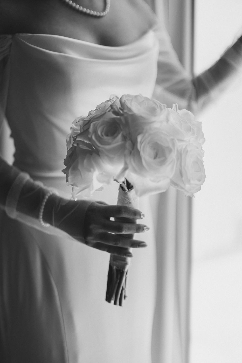 Artistic black and white photograph of white rose wedding bouquet in window light.