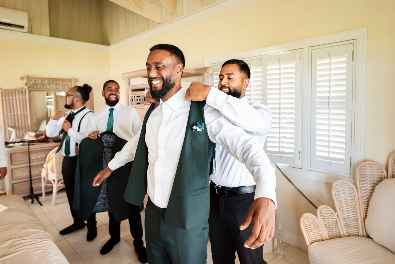 Groomsmen in white shirts and dark vests preparing in a bright interior room.