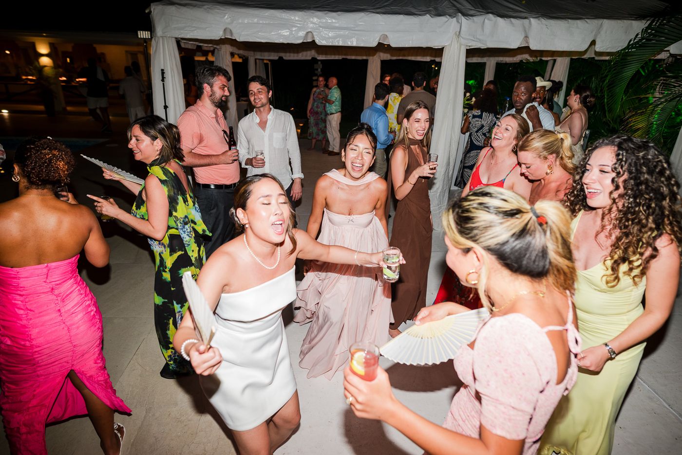 Party guests dance and celebrate under string lights at a tropical outdoor reception.