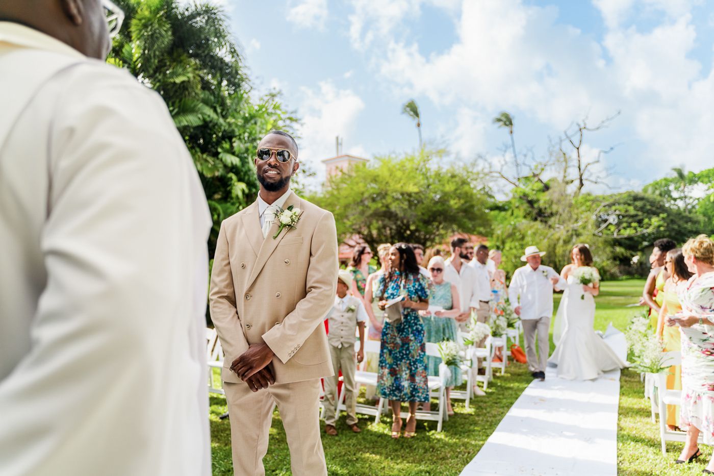 Wedding guests seated in white chairs during an outdoor ceremony in a tropical garden setting.