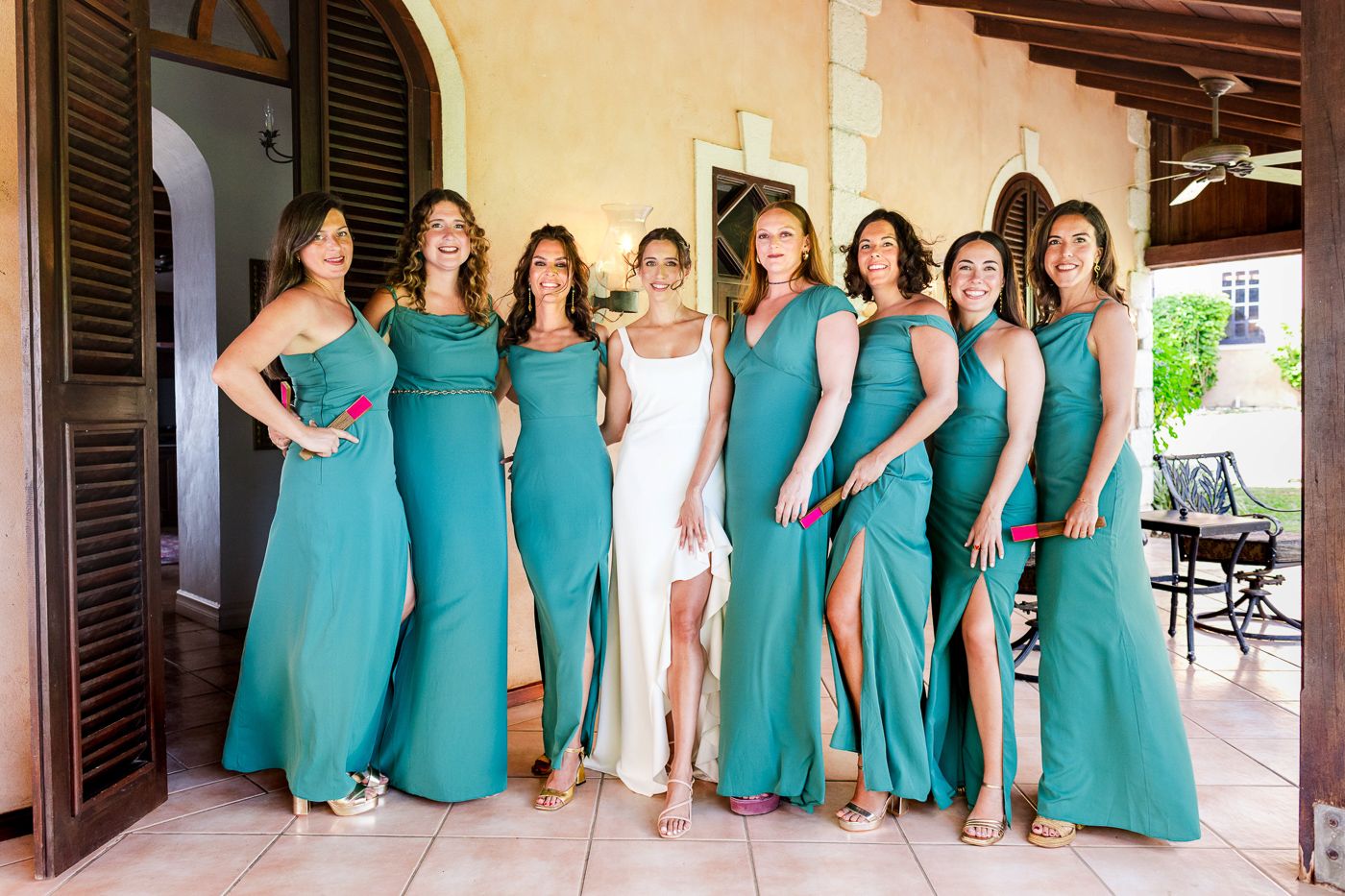 Wedding party in turquoise bridesmaid dresses lined up along a colonial style veranda.