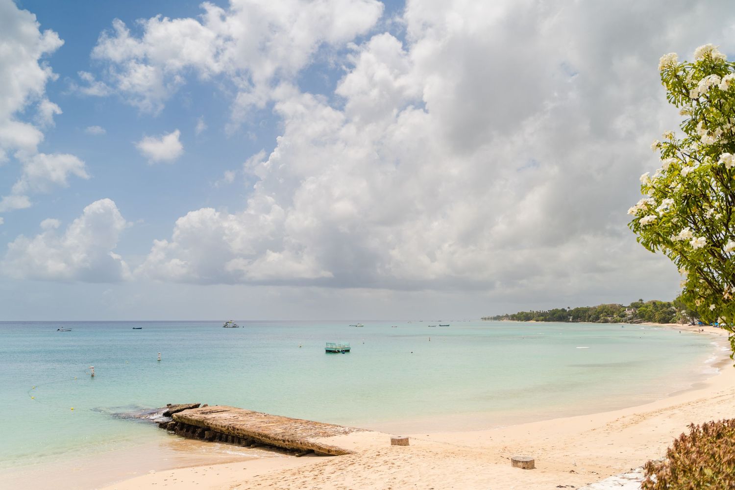 Tropical beach landscape with white sand and turquoise waters under cloudy skies.