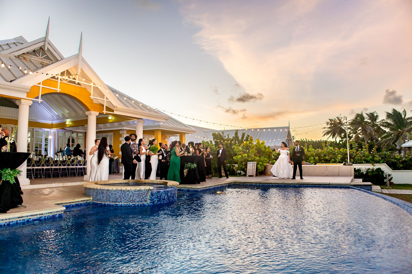 Panoramic view of a luxury beachfront venue with infinity pool and palm trees at sunset.
