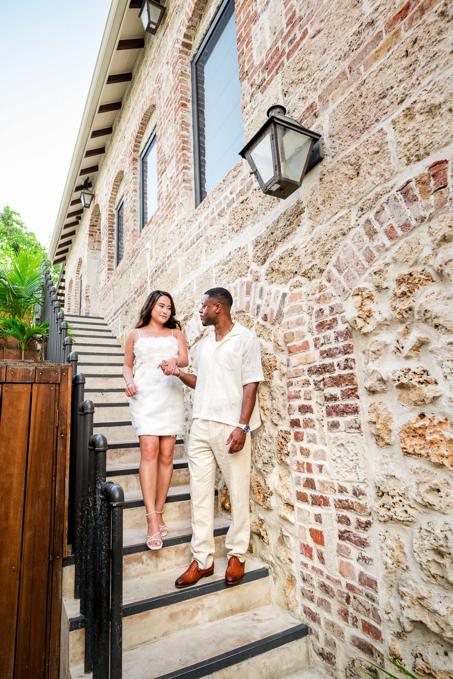 Couple posing on stone steps against a rustic brick wall exterior, barbados