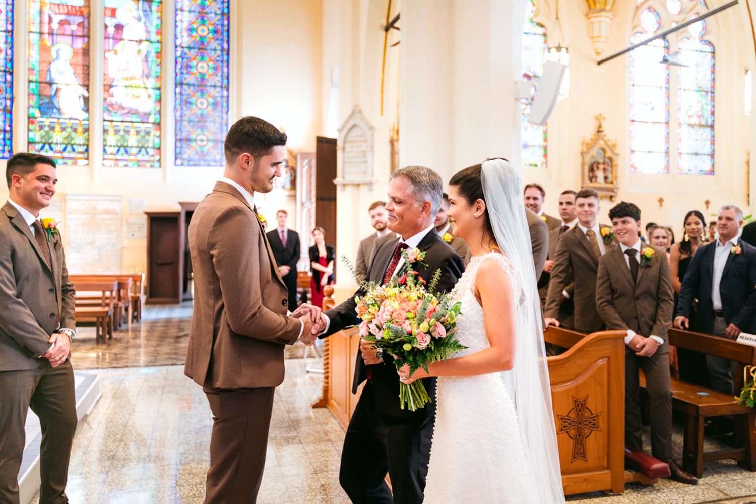 A bride and groom stand at the altar in a beautiful church with ornate stained glass windows during their wedding ceremony.