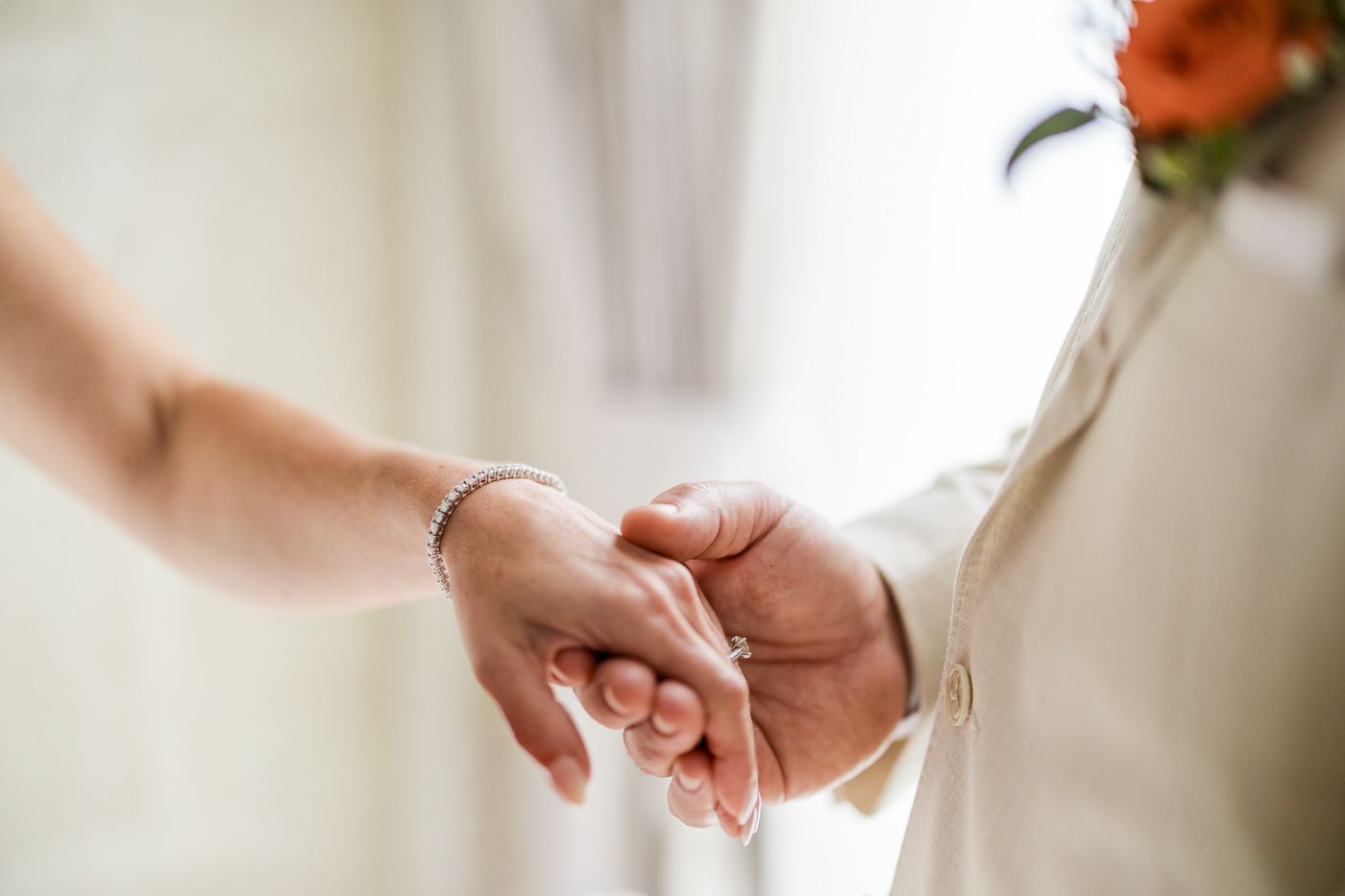 Close-up of a bride and groom holding hands, showcasing a delicate bracelet and wedding attire.