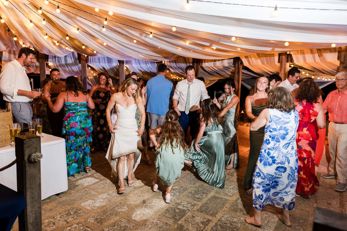 Guests dancing and socializing at an outdoor wedding reception under string lights and draped fabric canopy.