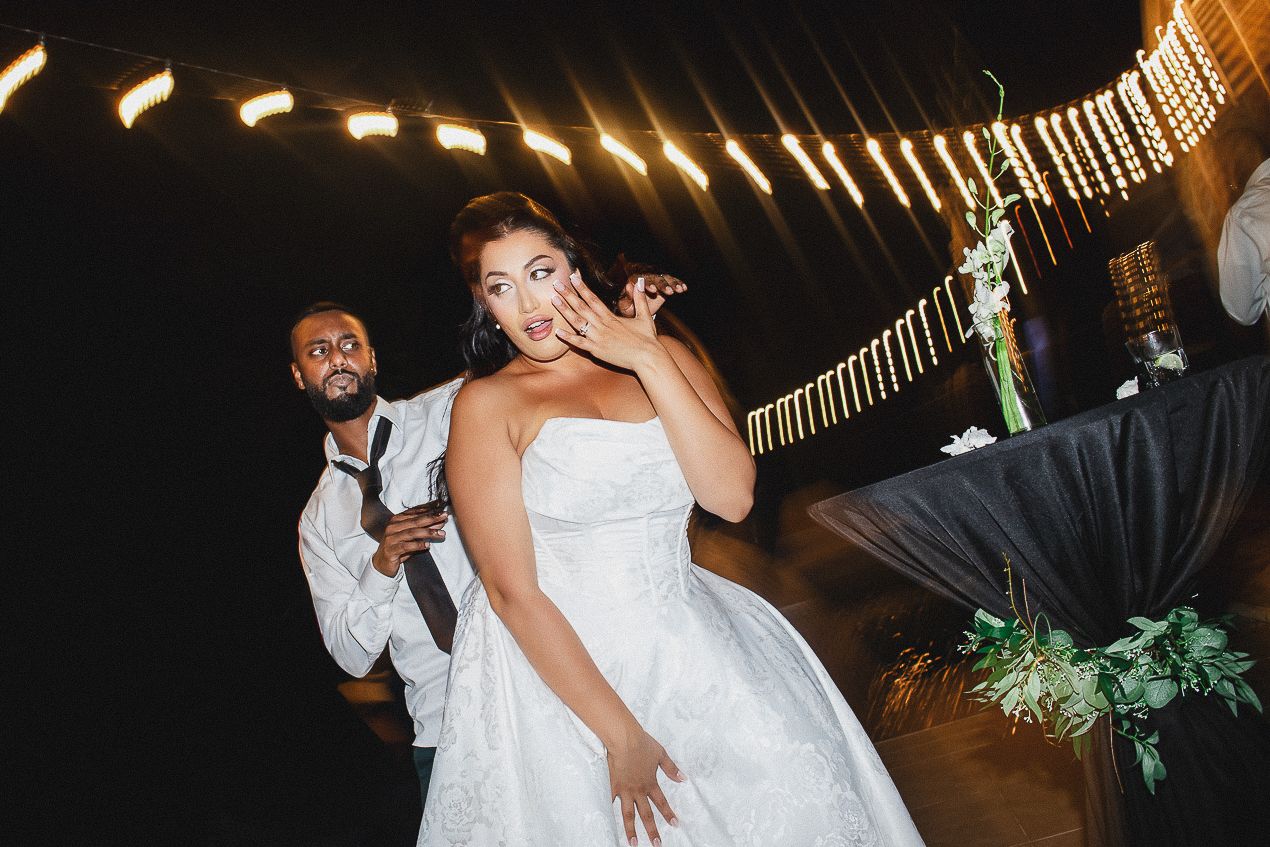 A couple dances together at their wedding reception in a dimly lit venue with romantic lighting.