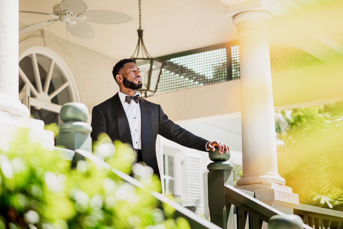 An elegant scene on a tropical veranda with someone in formal attire among lush greenery.