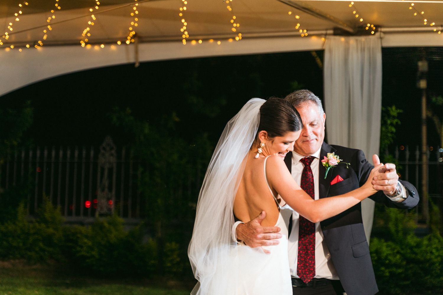 A couple dances together outdoors under string lights during their evening wedding celebration.