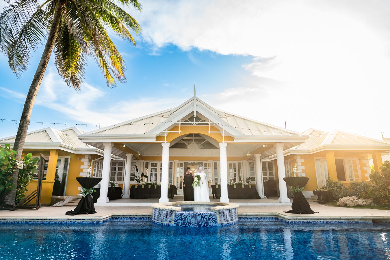 Luxury beachfront wedding venue with white pavilion and swimming pool at sunset.