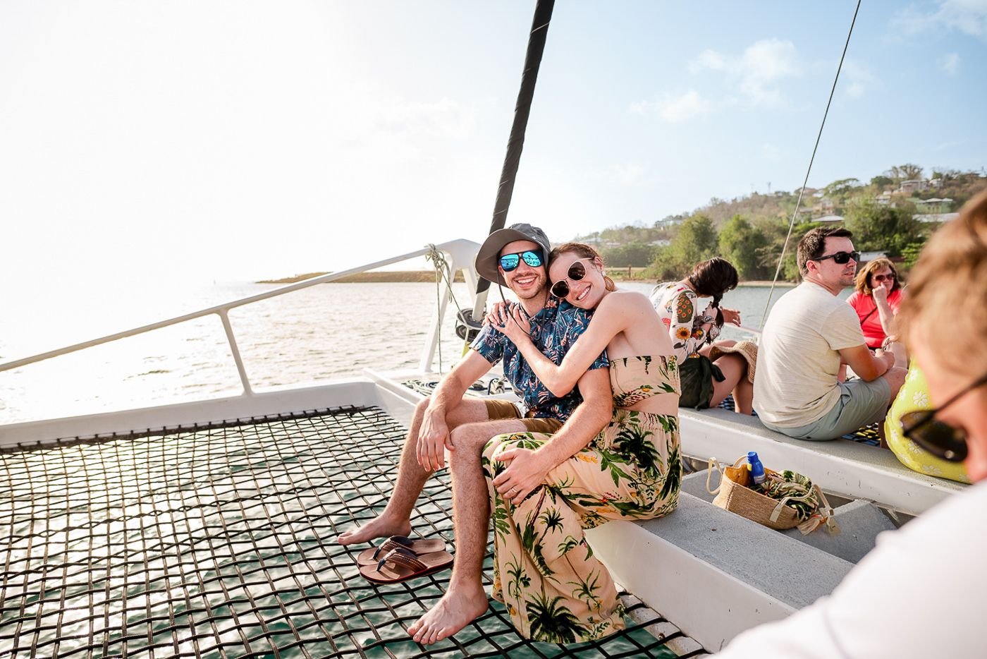 People lounging on the netting of a catamaran during a sunny day sail.