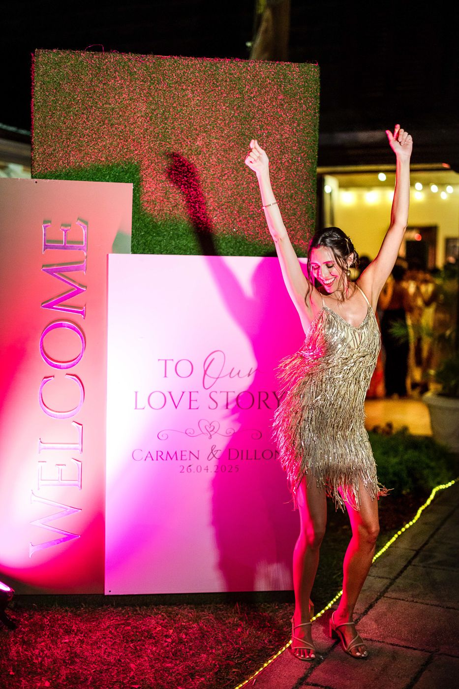 Pink illuminated signage and decorative elements at a nighttime outdoor celebration.