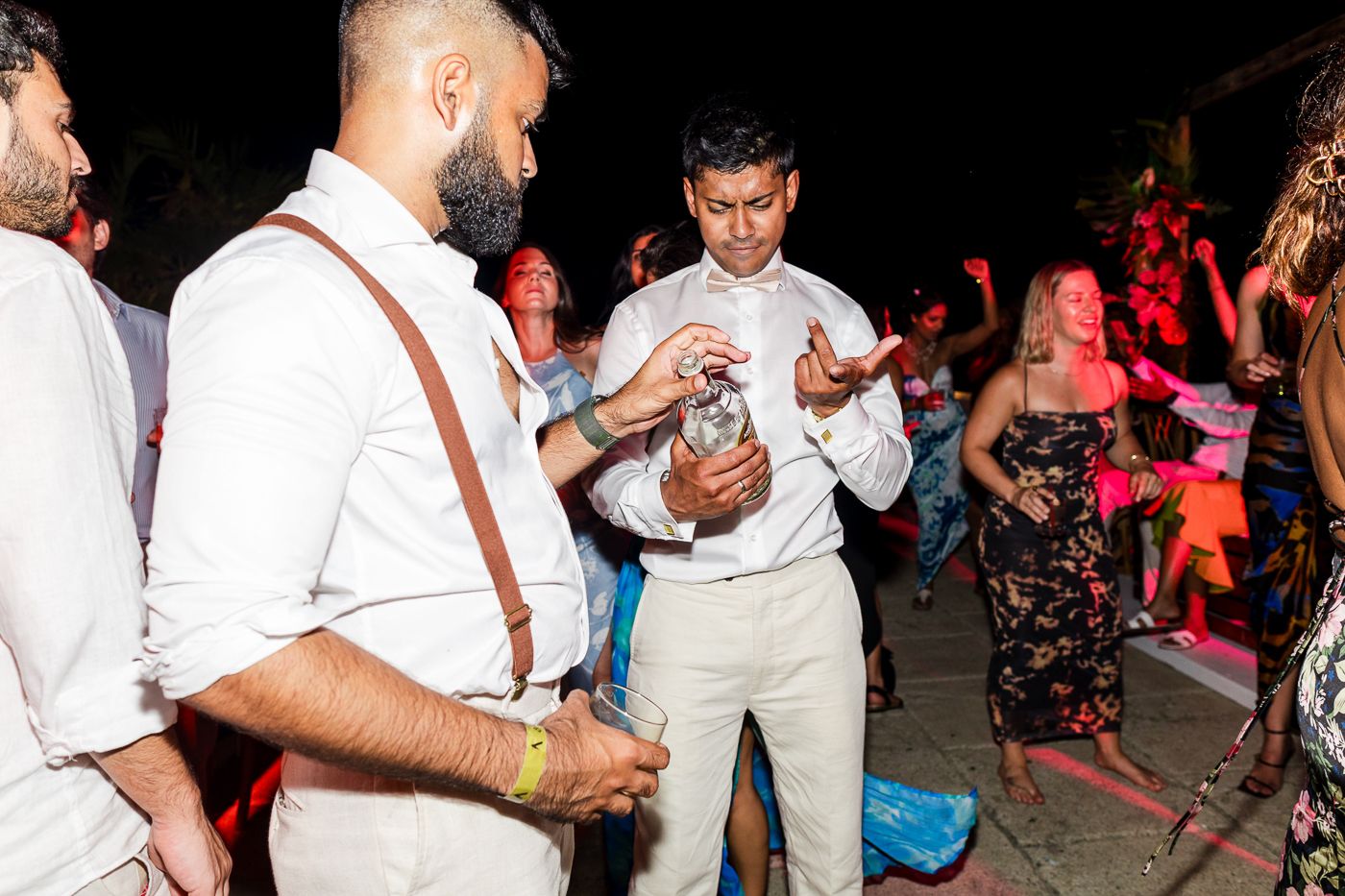 Party guests in white attire dancing and celebrating at a nighttime event.