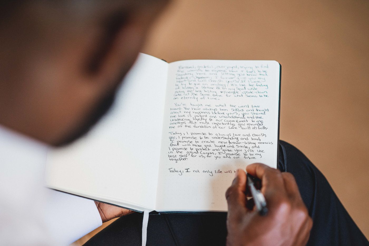 Close-up of hands writing in notebook with pen on white background.