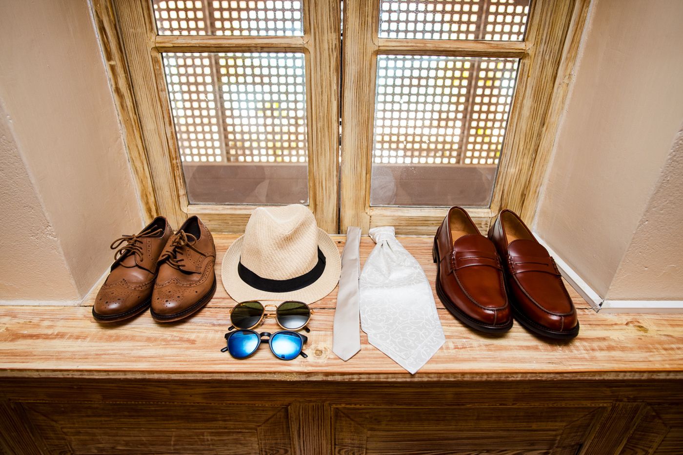 Wedding shoes and accessories arranged beneath a latticed window in warm natural light.