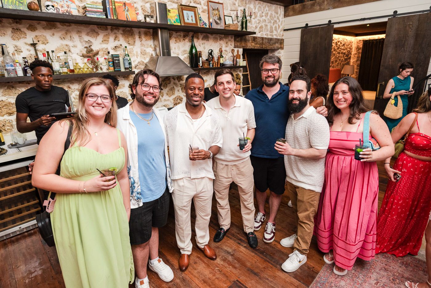 Group of party guests enjoying drinks and smiling at a rustic indoor bar venue.