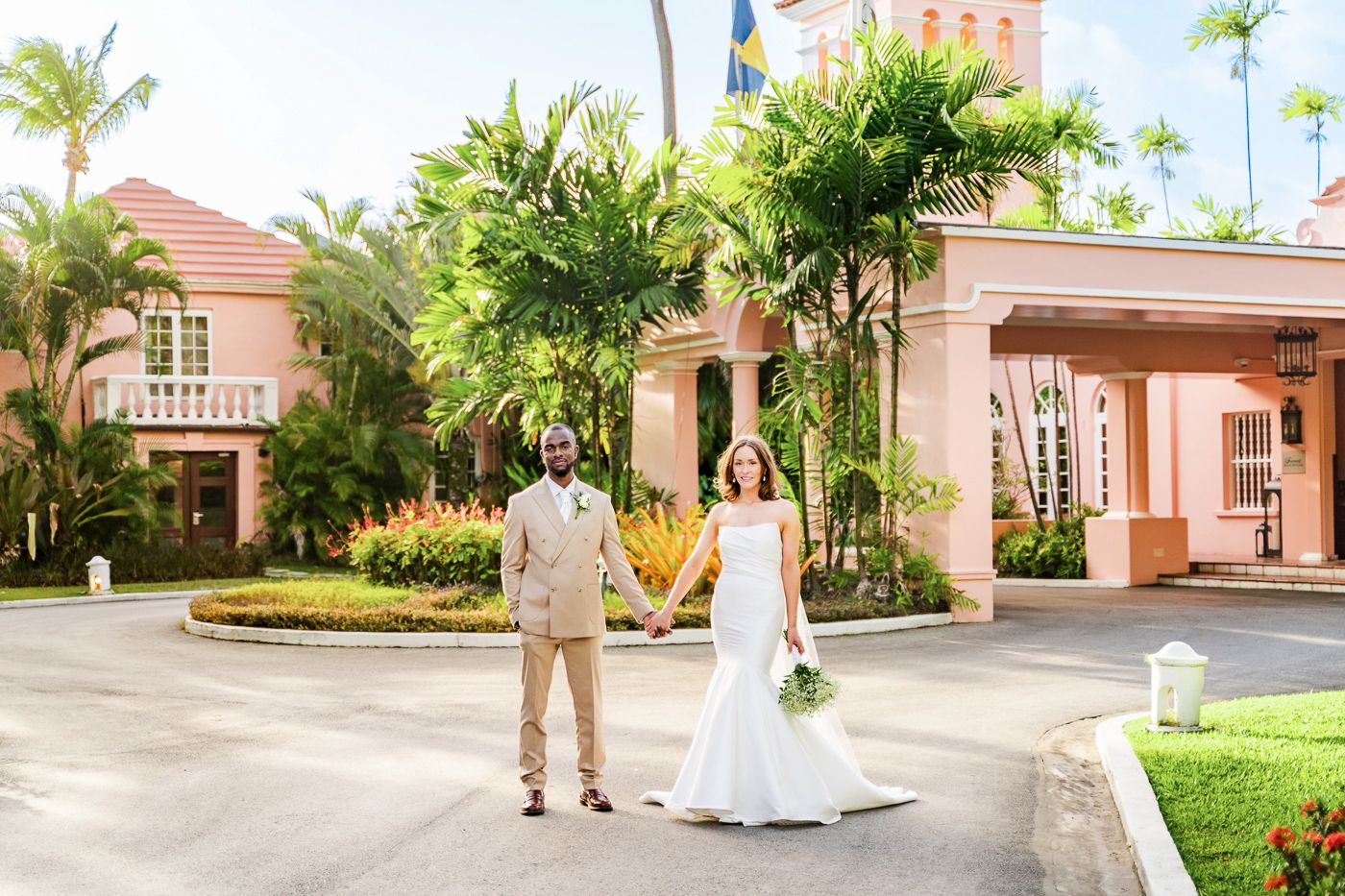 Bride and groom pose together outside pink Mediterranean style building.
