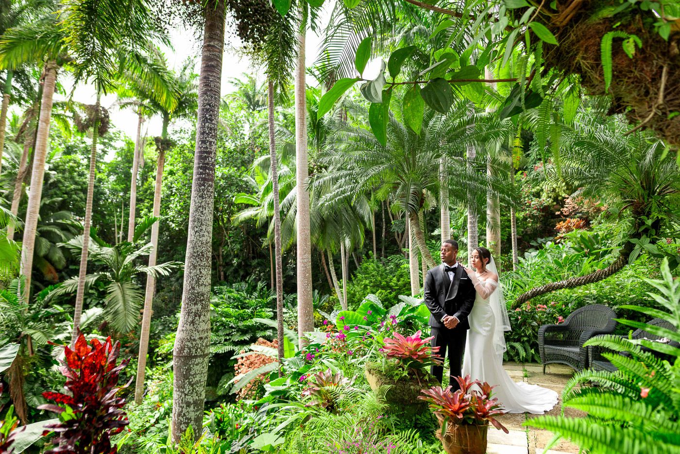 Panoramic view of a garden wedding ceremony surrounded by tropical palm trees and colorful flowers.