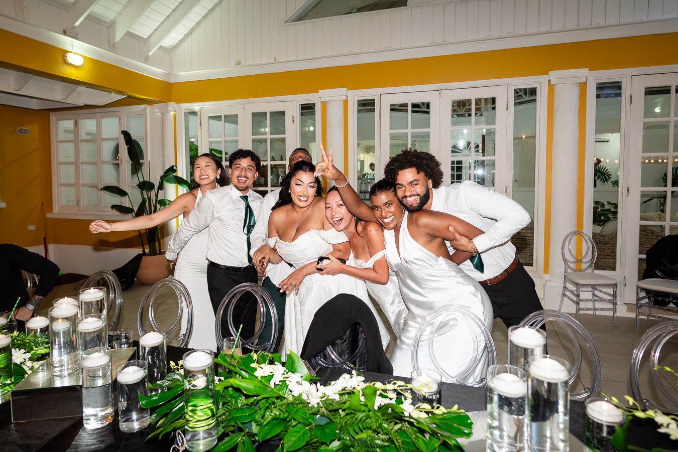 Wedding party poses playfully for a group photo in a bright indoor venue.