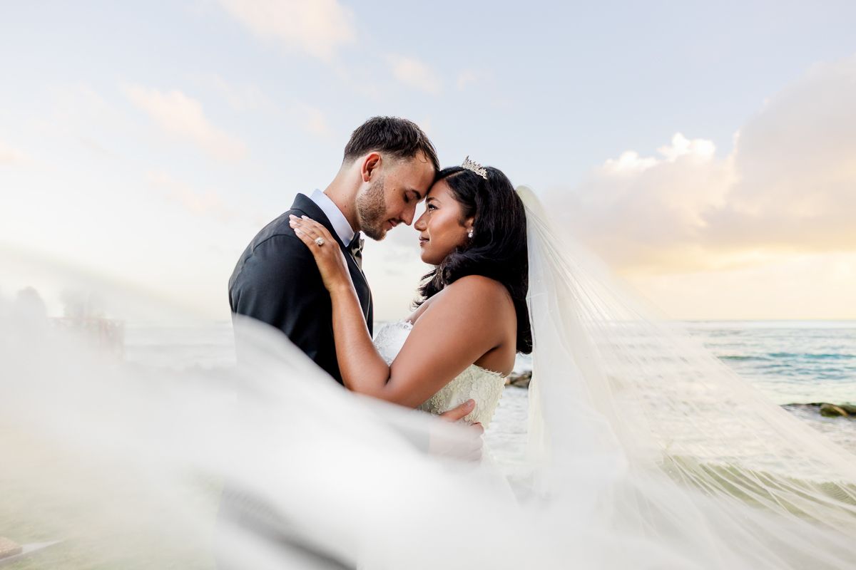 A romantic beach wedding couple embraces during sunset by the ocean waves.