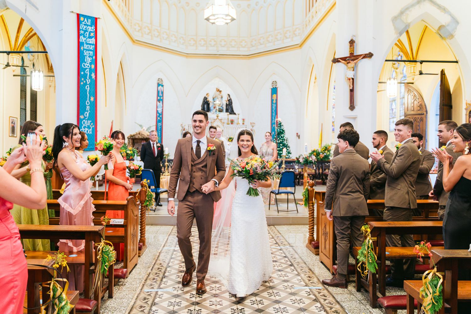 A couple walks down the church aisle after their wedding ceremony while guests take photos and celebrate.