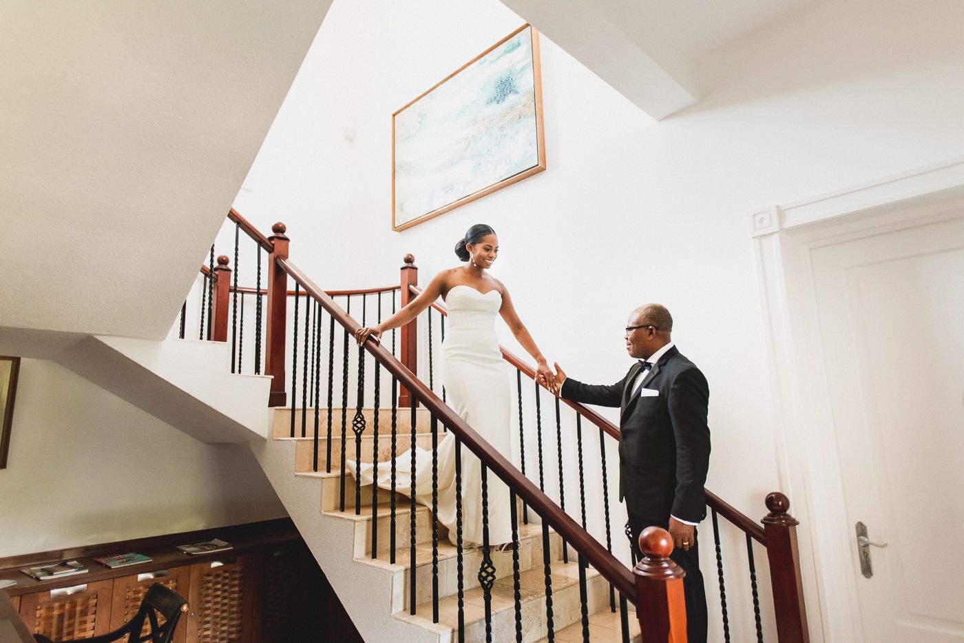Elegant staircase moment captured during a wedding at a classic indoor venue with wooden railings and white walls.