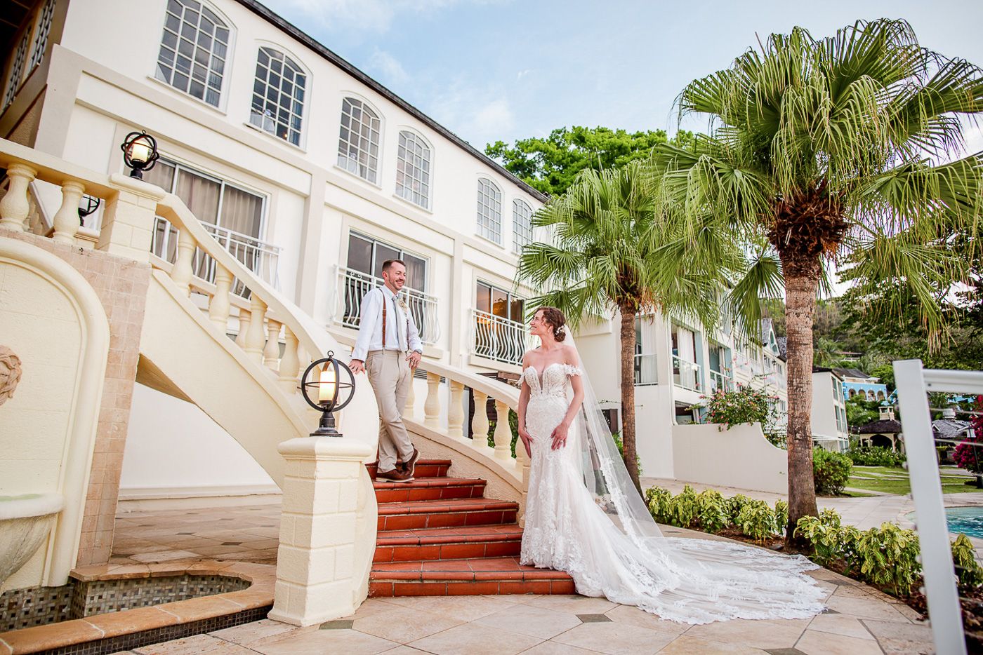 Elegant white mansion wedding venue with grand staircase and palm trees.