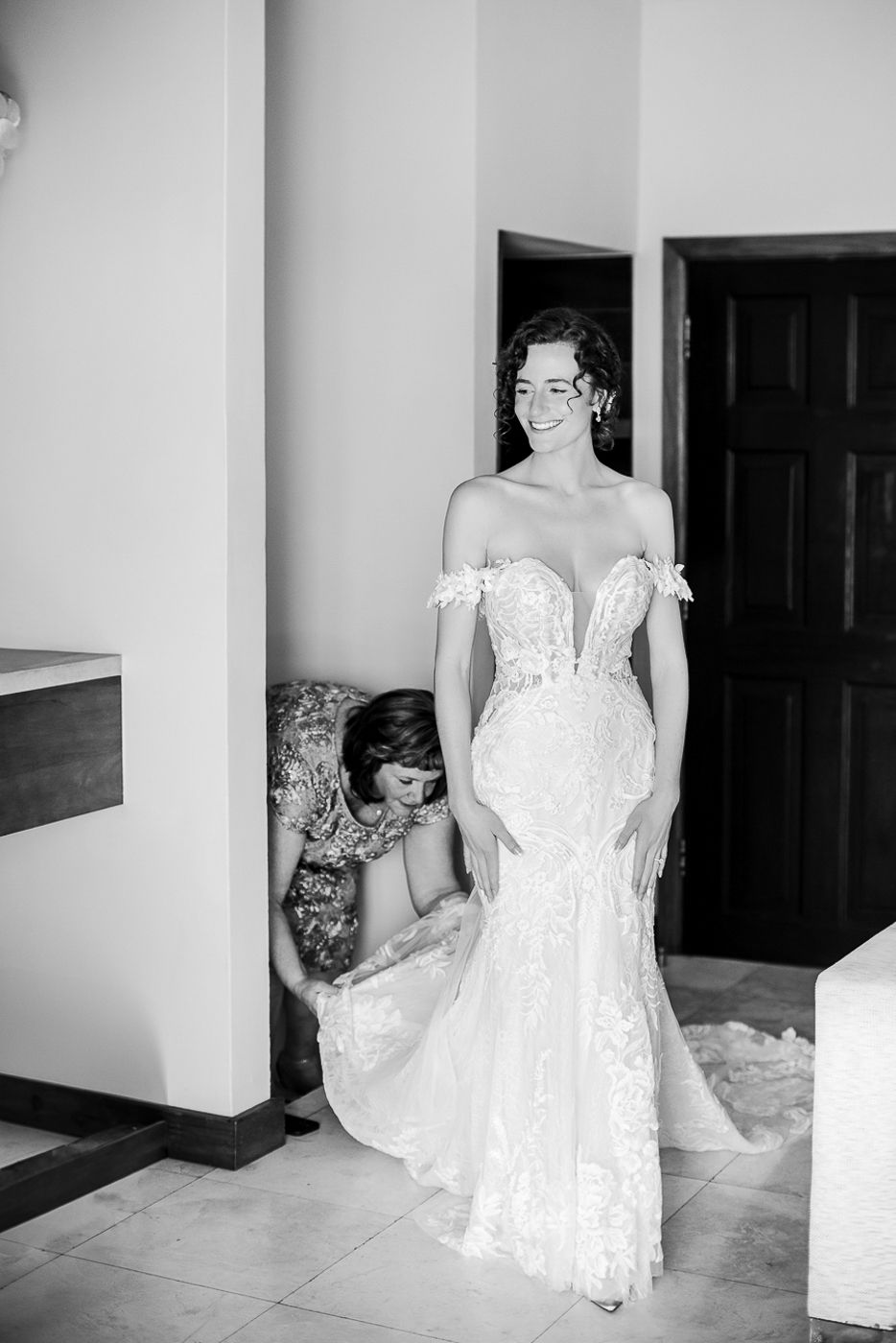 Elegant white lace wedding dress being adjusted in a minimalist interior setting.