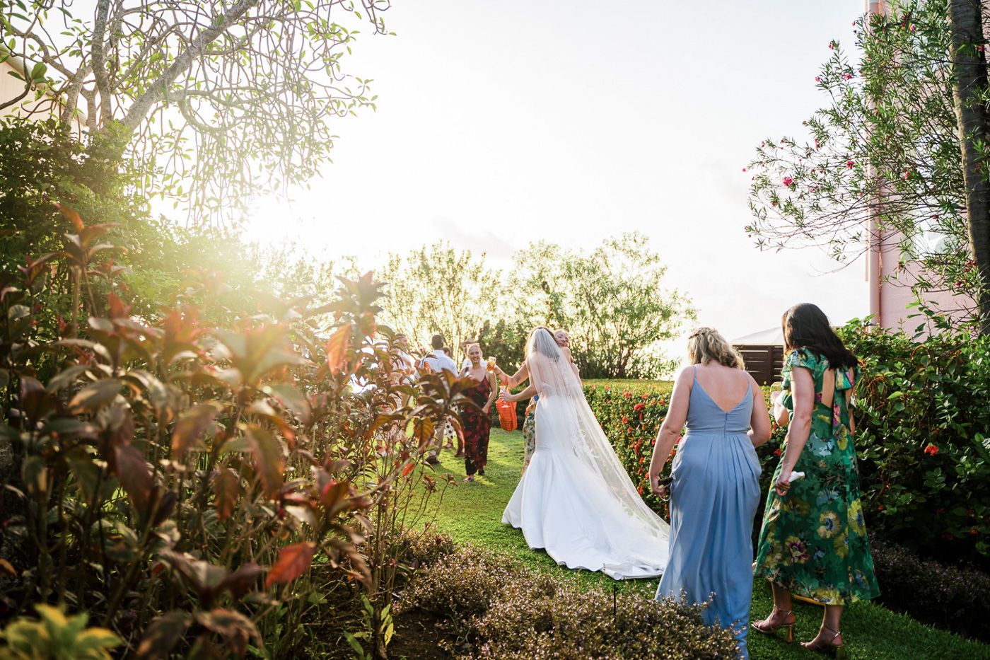Wedding guests gather in a lush garden setting during golden hour.