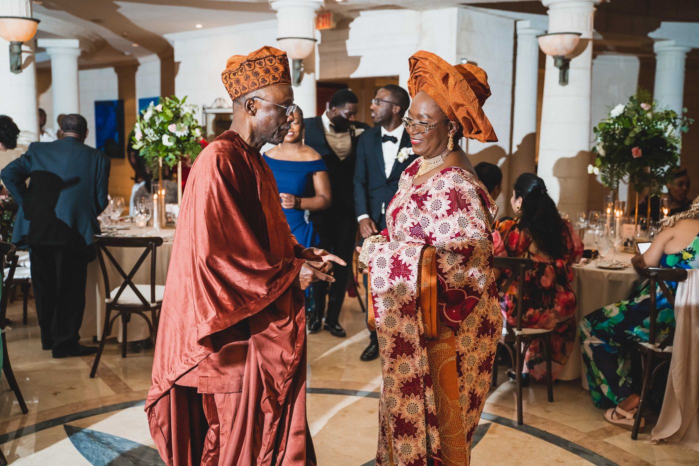 Wedding reception guests mingling in an elegant indoor venue with colonial-style pillars.