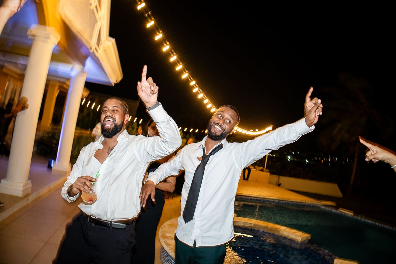 Two guests celebrating enthusiastically outdoors under string lights at night.