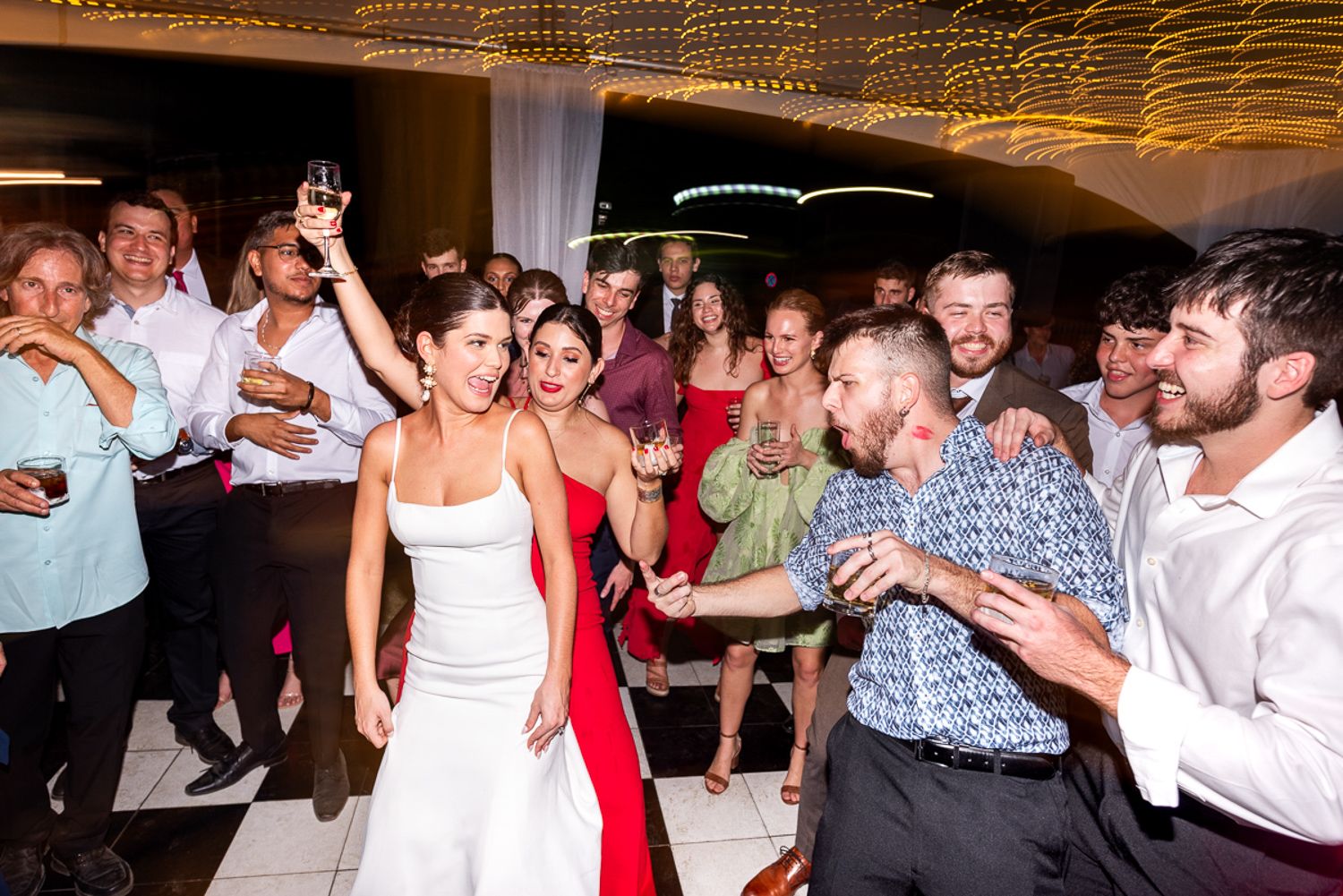 Festive dance party at a wedding reception with colorful lighting and energetic guests on the dance floor.
