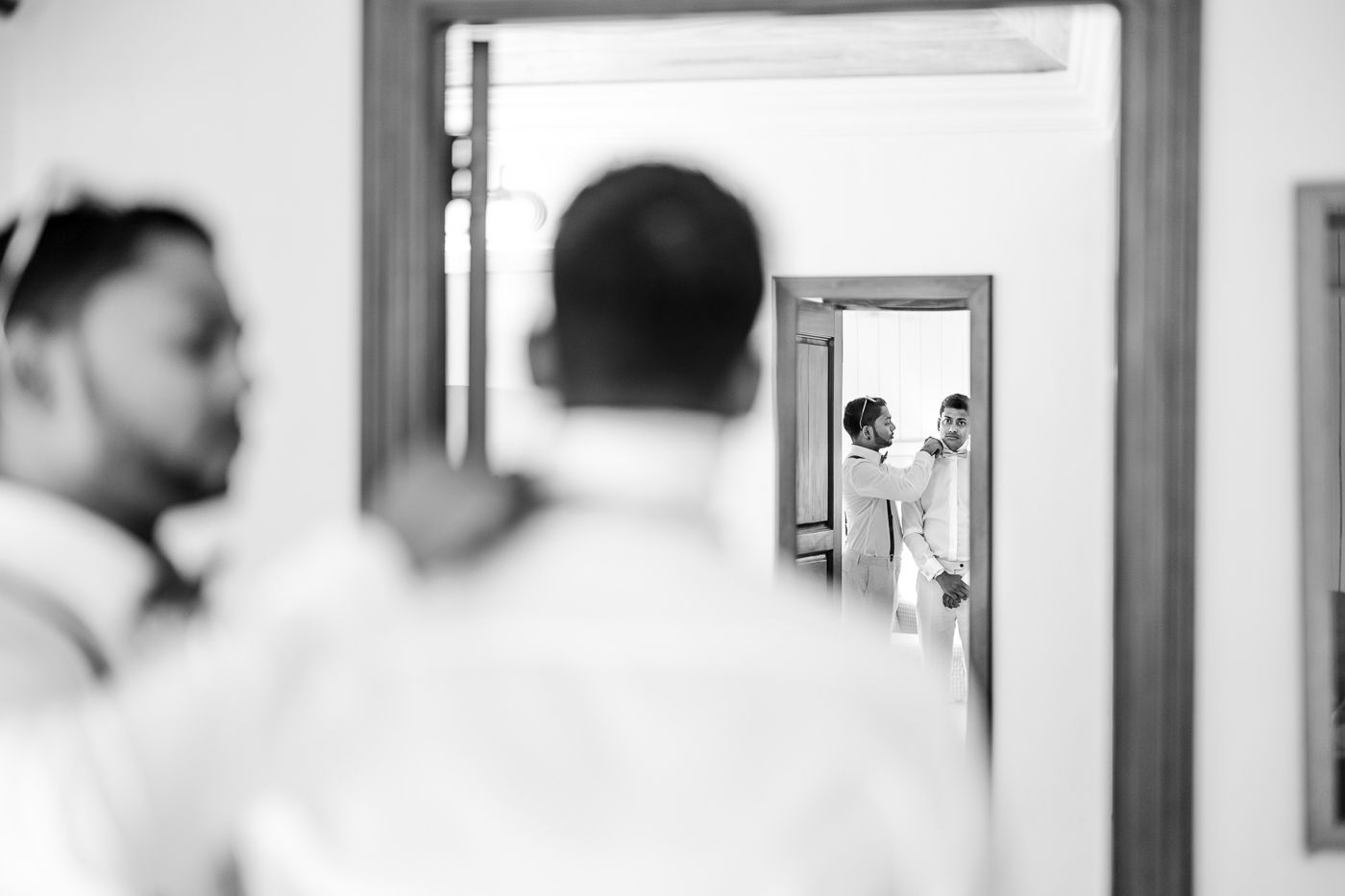 Black and white reflection of two people getting ready through multiple mirrors.