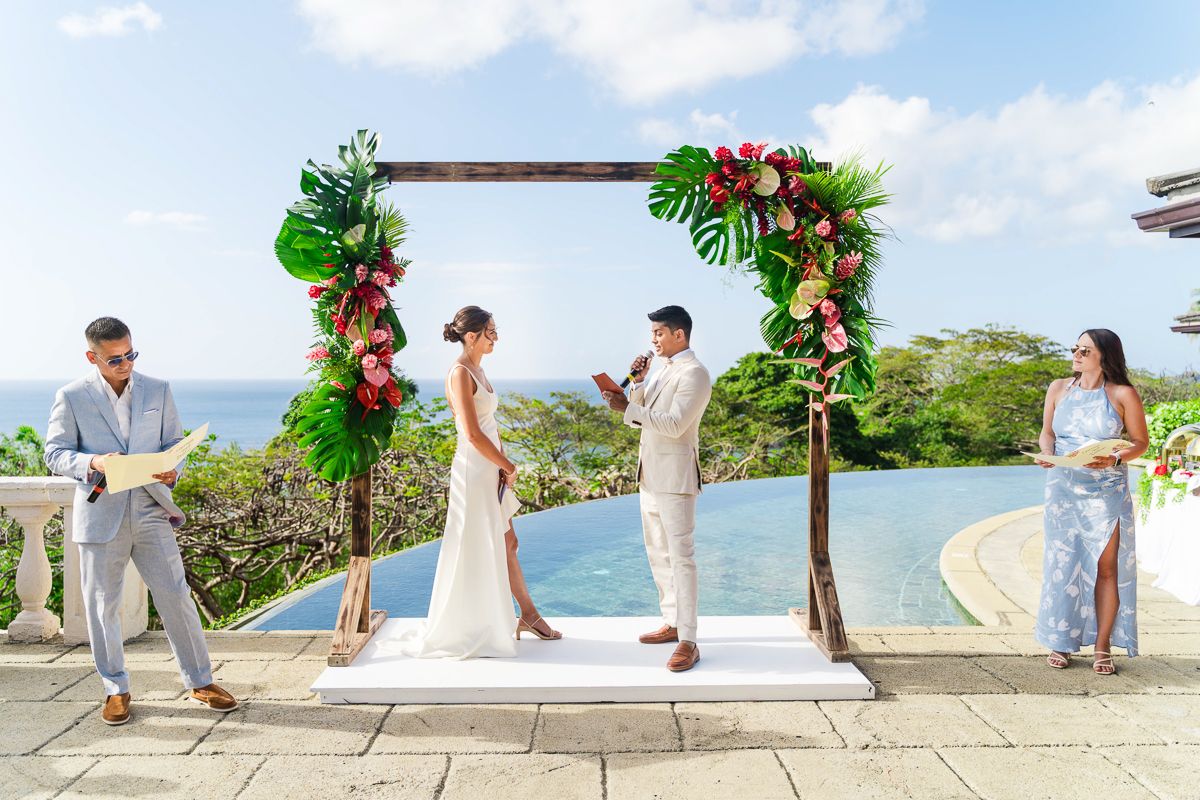 Tropical outdoor wedding ceremony under floral arch with pool and ocean view in Bali.