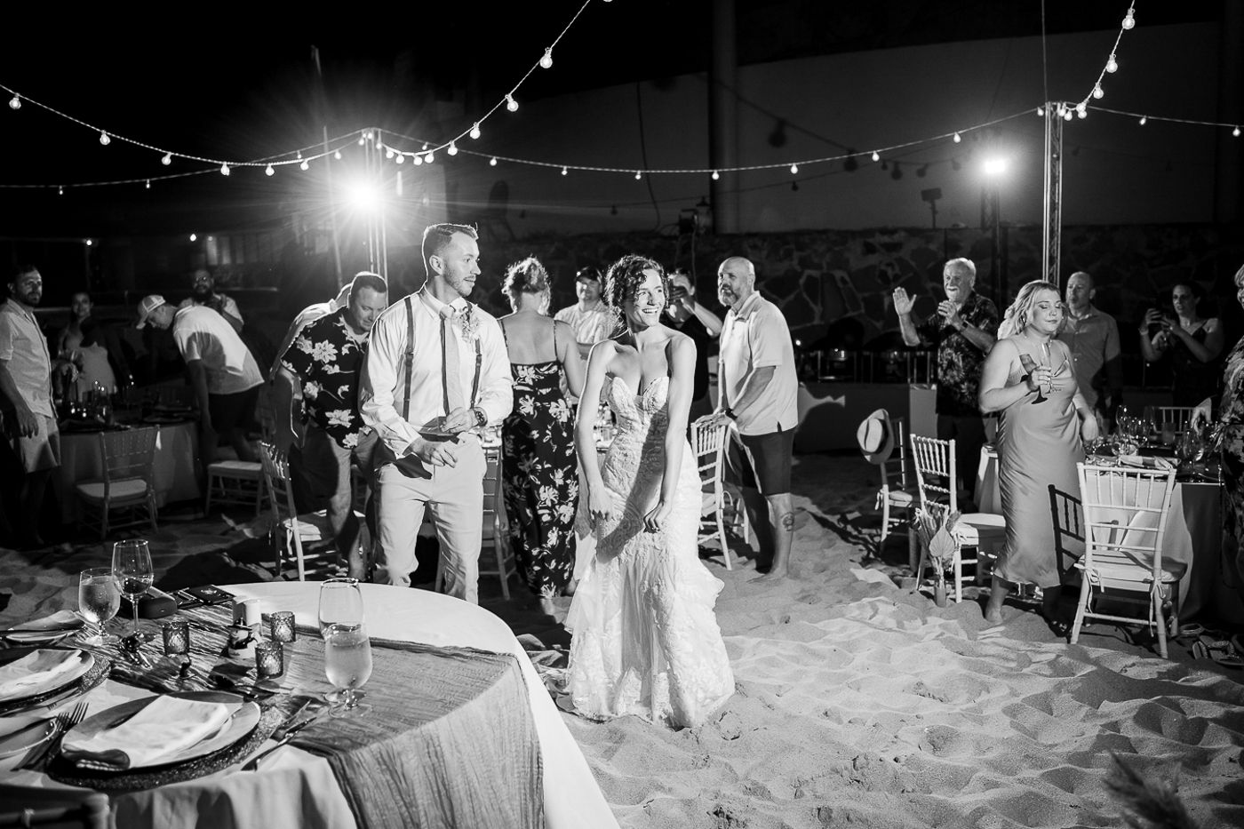 Beach wedding reception setup with string lights illuminating the sandy shore at night.