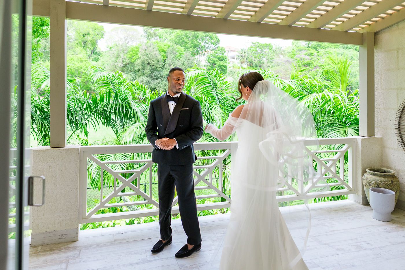 A couple shares a tender moment on an elegant white covered porch surrounded by lush greenery.