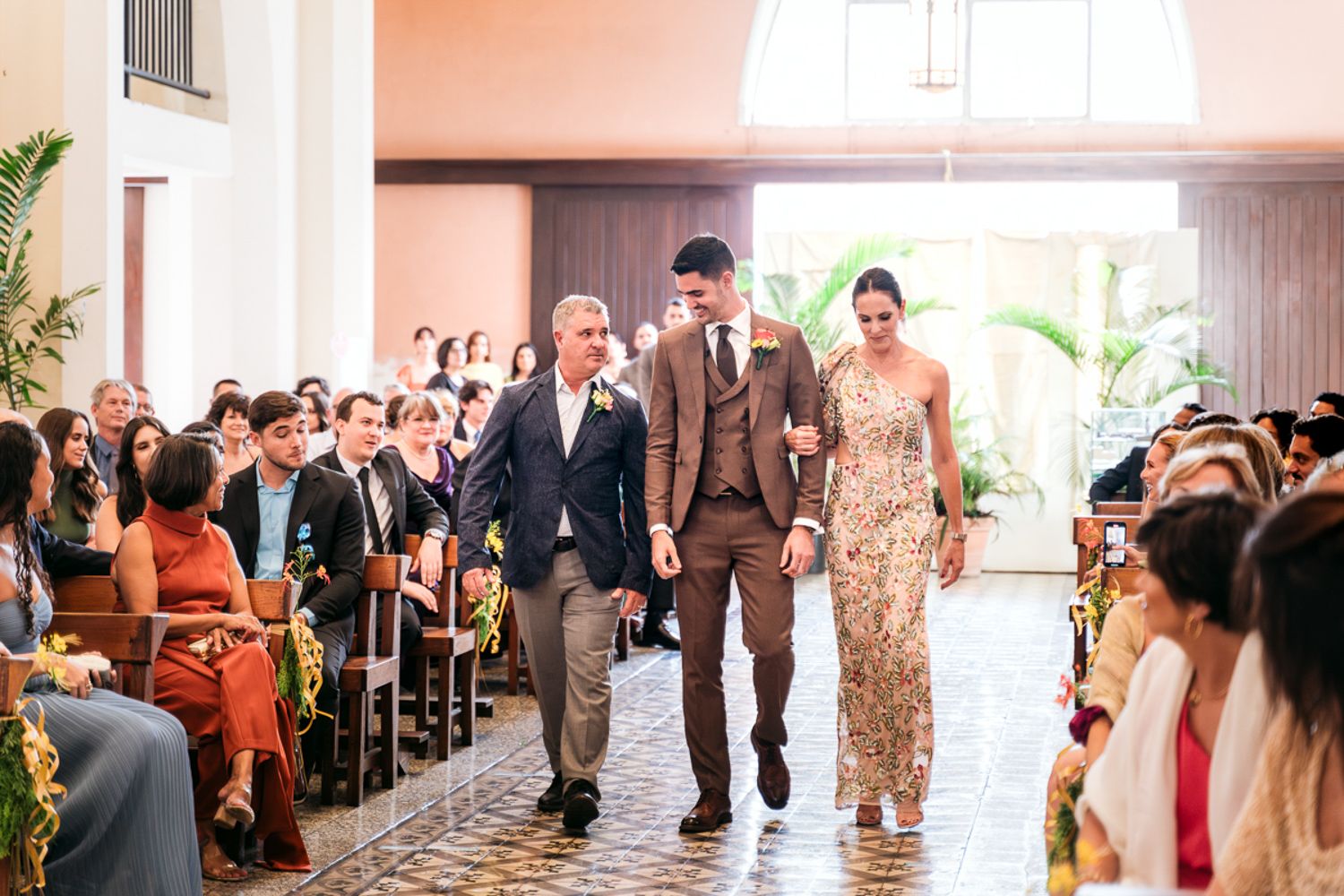 Wedding procession walking together down a church aisle lined with guests during a traditional ceremony.