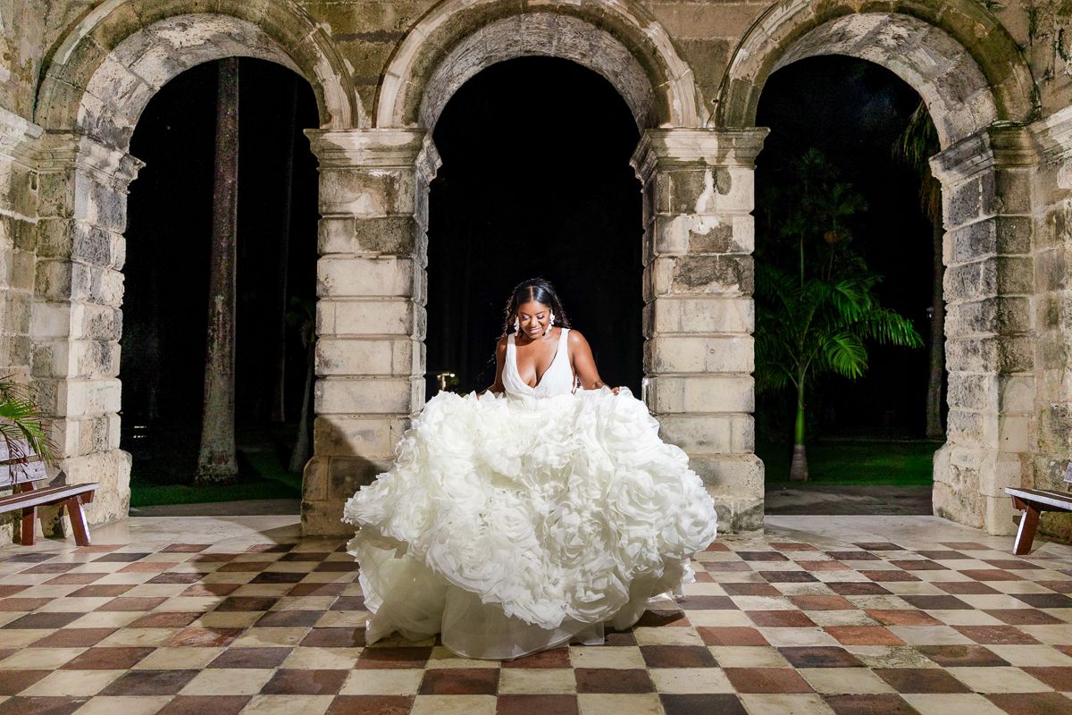 A couple in wedding attire poses under the stone archways of an ancient monastery with checkered floors.