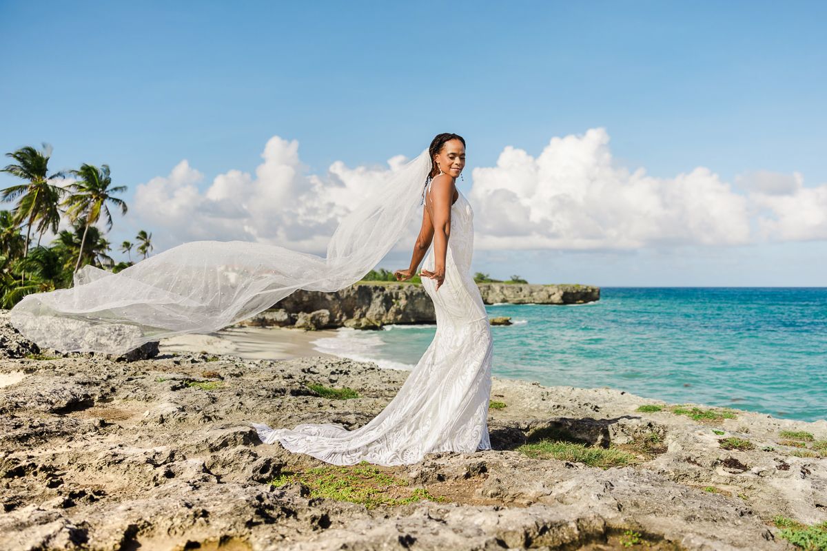 A stunning coastal wedding photo shoot with turquoise waters, palm trees, and rocky cliffs along a tropical beach.