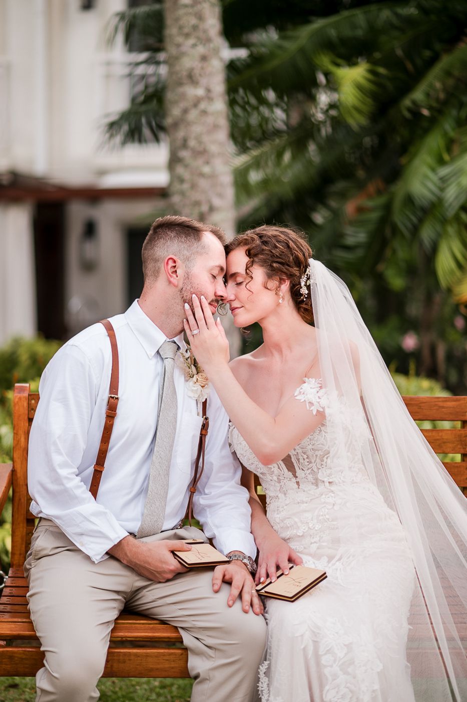 Intimate wedding moments captured on wooden bench in tropical garden setting.