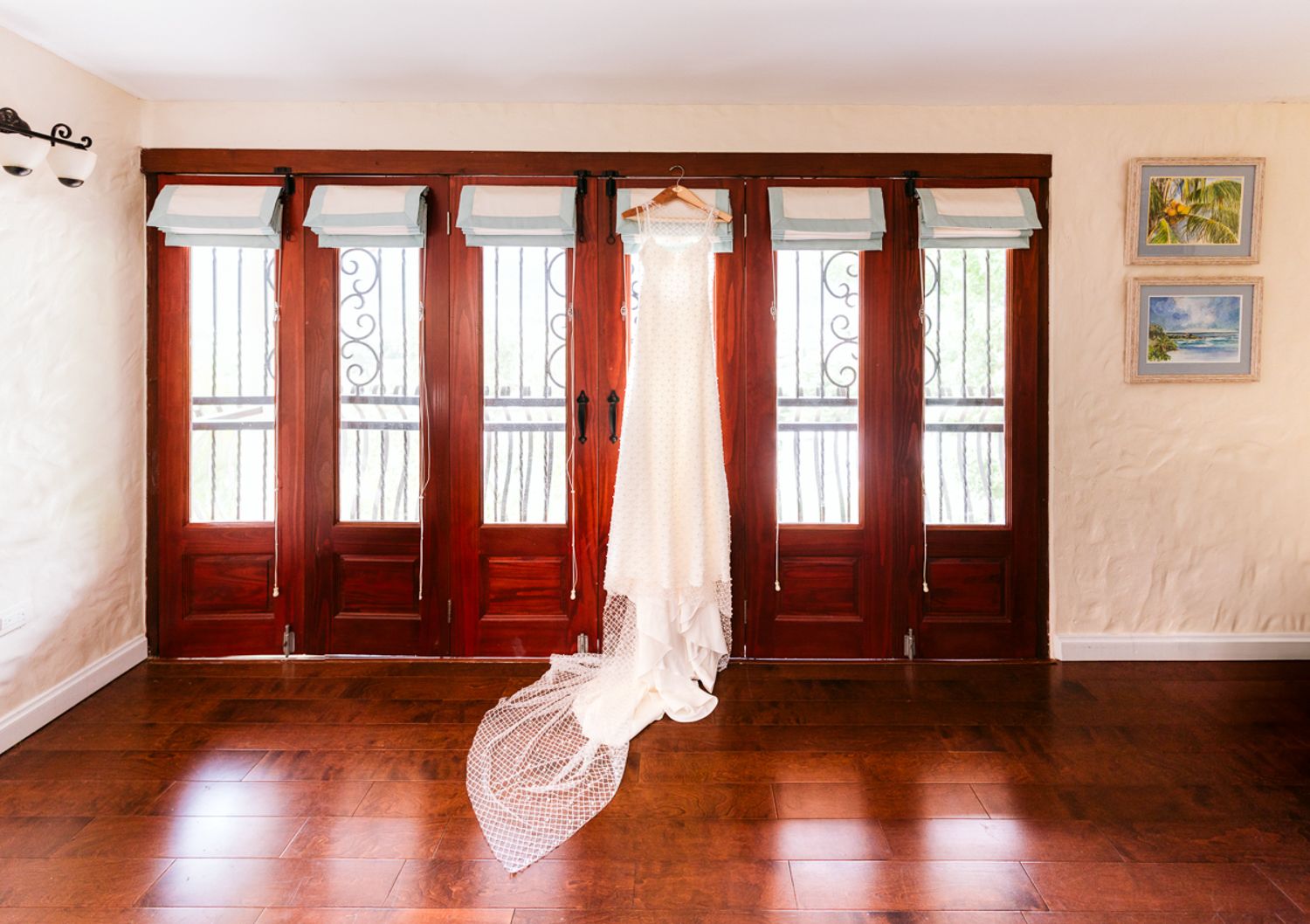 A white curtain billows gently near a window in a room with hardwood floors and warm wood trim details.