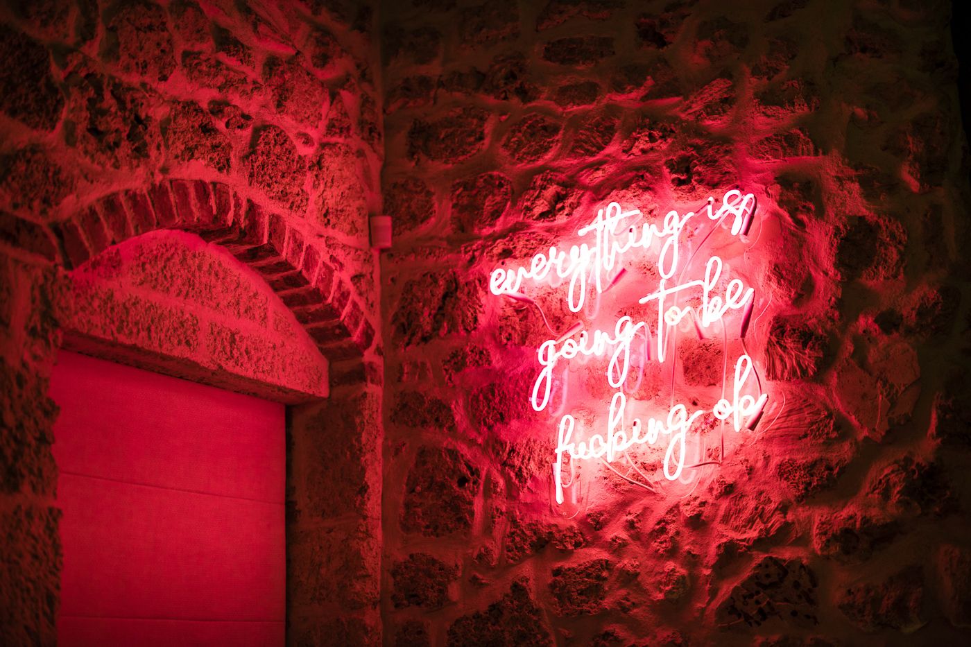 Red neon sign glowing on a textured stone wall at an event venue.