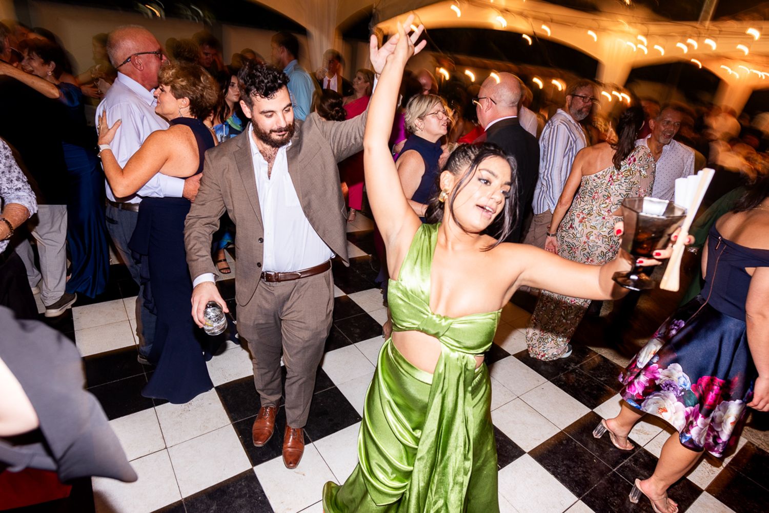 People dancing and celebrating together on a dance floor at an indoor event space with festive lighting.
